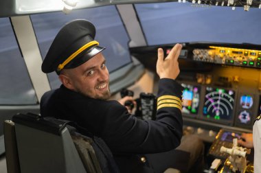 Uçuş simülatörü kullanırken gülümseyen beyaz sakallı bir adam. Pilot kokpitte baş parmak gösteriyor.