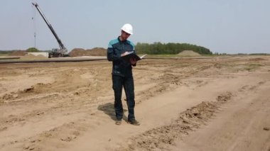 Miğferli bir adam inşaat alanında teknik denetim yapıyor. Drone videosu