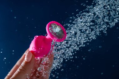 Duşun altında mavi arka planda pembe anal tıkaçları yıkayan kadın.