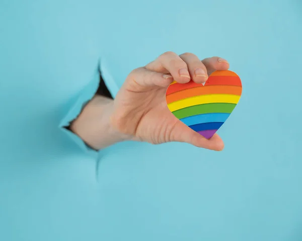 Hand Rainbow Colored Heart Sticking Out Hole Blue Cardboard Background — Foto de Stock