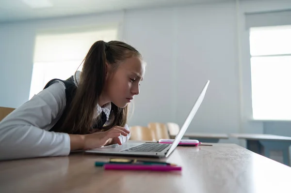 stock image Caucasian girl sits at a desk at school and carefully looks into a laptop