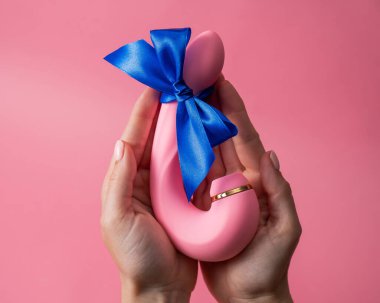 Woman holding curved dildo with blue ribbon on pink background. Copy space