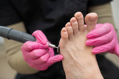 Bir pedikür uzmanı, güzellik salonunda aşındırıcı diski olan bir makine kullanan bir müşterinin ayak parmaklarını tedavi eder.