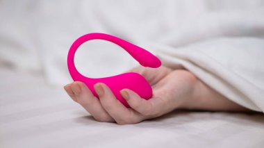 Yatakta uzanırken kavisli pembe vibratör tutan kadın.