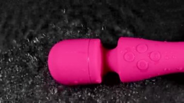 The pink dildo creates a vibration on the surface of the water. Sex toy on a black background