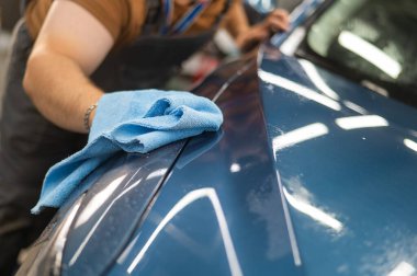 Bir araba servisinde usta koruyucu zırh filmi uyguladıktan sonra bir arabayı peçeteyle siler.