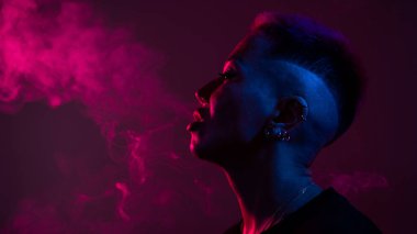 Kısa saçlı, neon ışıkta sigara içen Asyalı kadın profili