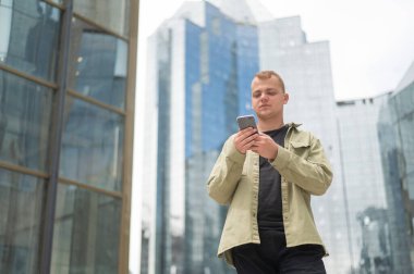 Genç beyaz adam şehir merkezinde akıllı telefon kullanıyor.