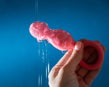 Mavi arka planda pembe anal boncuklara kayganlaştırıcı döken kadın.