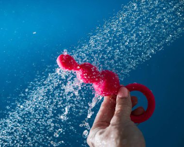 Mavi arka planda akan suyun altında pembe anal boncuklar tutan bir kadın. Seks oyuncağı hijyen konsepti