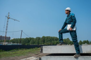 İnşaat alanında elinde dizüstü bilgisayar tutan beyaz erkek müteahhit.