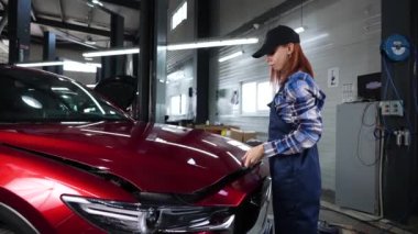 Kadın oto tamircisi araba servisinde arabanın kaputunu kapatıyor.