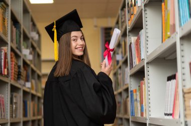 Mezuniyet elbisesi içinde, elinde diploması olan mutlu genç bir kadın.