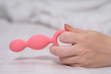 Yatakta uzanmış pembe anal boncuklu bir kadının yakın çekimi.