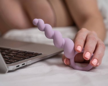 Yatakta yatarken dizüstü bilgisayarın yanında leylak anal boncuklar tutan kadın.