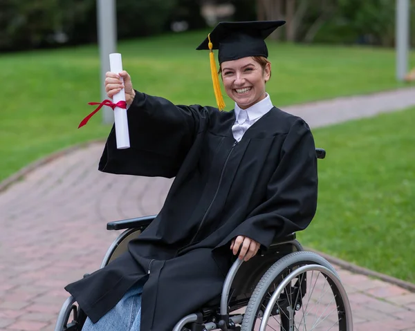 stock image Caucasian woman in a wheelchair in a graduate costume rejoices at receiving a diploma