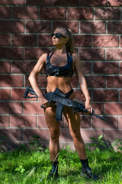 Bikinili Beyaz Bir Kadın Bir Makineli Tüfeği Tuğla Duvara Dayadı — Stok fotoğraf