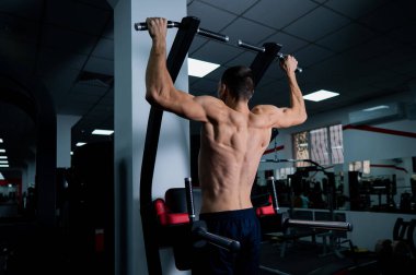 Back view of shirtless man with pull-ups in gym
