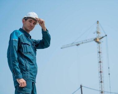 İş kıyafetleri ve kask giymiş bir müteahhit inşaat sahasının arka planında duruyor.