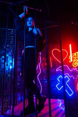 Çelik parmaklıkların arkasındaki neon stüdyodaki beyaz kadın.