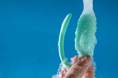 Bir kadın mavi arka planda akan suyun altında vibratör yıkıyor. Kadın Sağlığı Kegel Eğitmeni