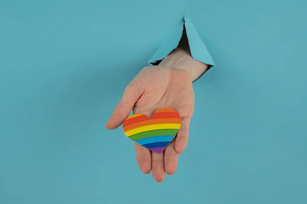 Hand Rainbow Colored Heart Sticking Out Hole Blue Cardboard Background —  Fotos de Stock