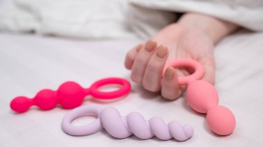 Bir kadın yatakta yatarken bir setten anal boncuk seçer.