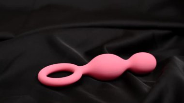 Kadın anal boncukları alıyor ve siyah ipek çarşafın altına çekiyor.