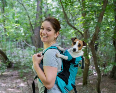 Beyaz bir kadın özel bir sırt çantasıyla köpek Jack Russell Terrier ile dışarı çıkıyor.