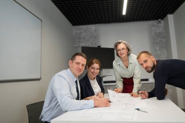 Tasarımcılar bir toplantıda çizimleri tartışırlar. Dört gülümseyen iş adamı kameraya bakıyor.