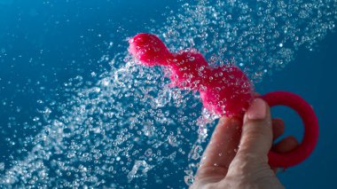 Mavi arka planda akan suyun altında pembe anal boncuklar tutan bir kadın. Seks oyuncağı hijyen konsepti