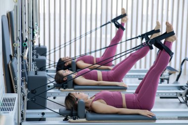 Pembe spor kıyafetli üç Asyalı kadın ıslah yatağıyla pilates egzersizi yapıyor.