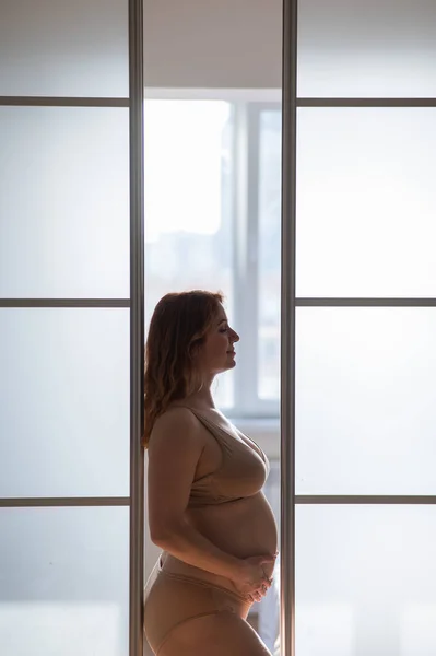 stock image A pregnant woman in nude lingerie stands in profile between folding doors