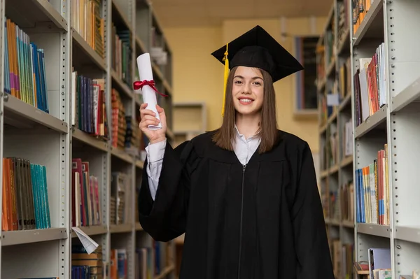 Счастливая Молодая Женщина Выпускном Платье Держит Диплом Библиотеке — стоковое фото