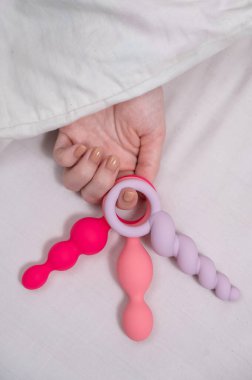 Yatakta yatarken elinde üç farklı anal boncuk tutan kadın.