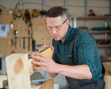 Marangoz atölyedeki tahtaları ölçer.