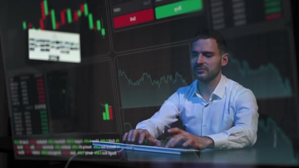 白人男性は仮想スクリーンの前に暗闇の中に座り キーボードに入力します 株式チャート — ストック動画