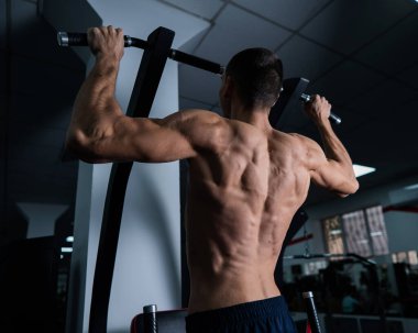 Back view of shirtless man with pull-ups in gym