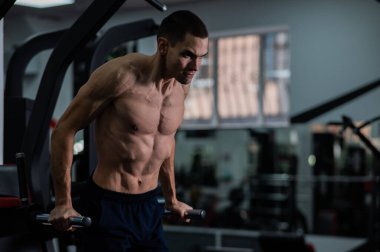 Shirtless man doing triceps dips from parallel bars in gym