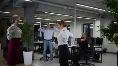 Four office workers warm up during a break. Employees do fitness exercises at the workplace. Slow motion