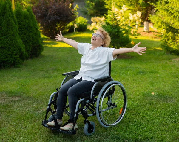 快乐的老妇人坐在轮椅上散步时 把胳膊伸向两边 — 图库照片