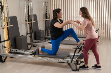 Aşırı kilolu beyaz kadın kişisel antrenörle pilates egzersizi yapıyor.