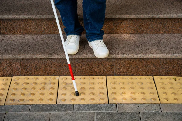 Close-up of female foot, walking stick and tactile tiles. Blind woman walking down stairs using a cane