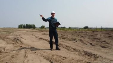 Miğferli bir adam inşaat alanında teknik denetim yapıyor. Drone videosu