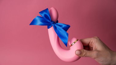 Woman holding curved dildo with blue ribbon on pink background. Copy space