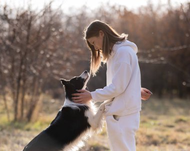 Beyaz kadın sonbahar parkında bankta otururken köpeğine sarılıyor.