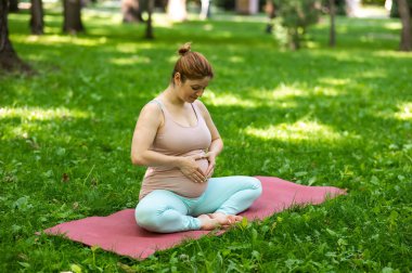 Doğum öncesi yoga. Beyaz hamile kadın parkta kelebek pozu veriyor.