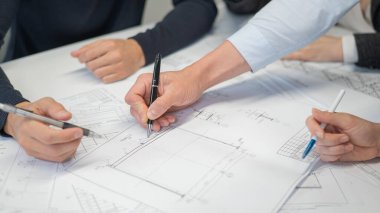 Ofisteki masanın üzerinde planları olan dört meslektaşın ellerinin yakın çekimi. Mühendis ve mimarların beyin fırtınası