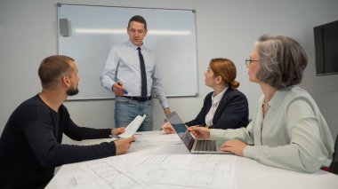 Caucasian man leading a presentation to colleagues at a white board