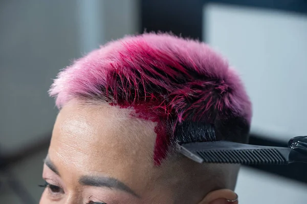 进程的密切关注 理发师把亚洲女人的头发染成粉色 短短的极端发型 — 图库照片